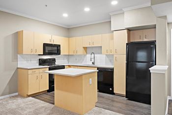 an empty kitchen with black appliances and wooden cabinets at Artisan Apartments & Shops, Austin, Texas